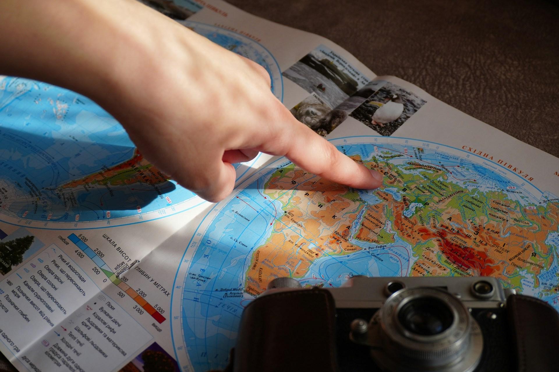 Hand zeigt auf Weltkarte bei der Routenplanung für Multistop-Reisen