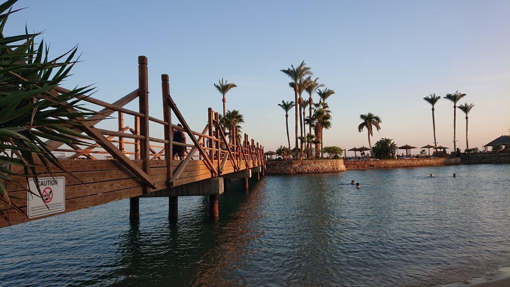 Holzbrücke über türkises Wasser zur Insel des Marriott Beach Resort mit Palmen