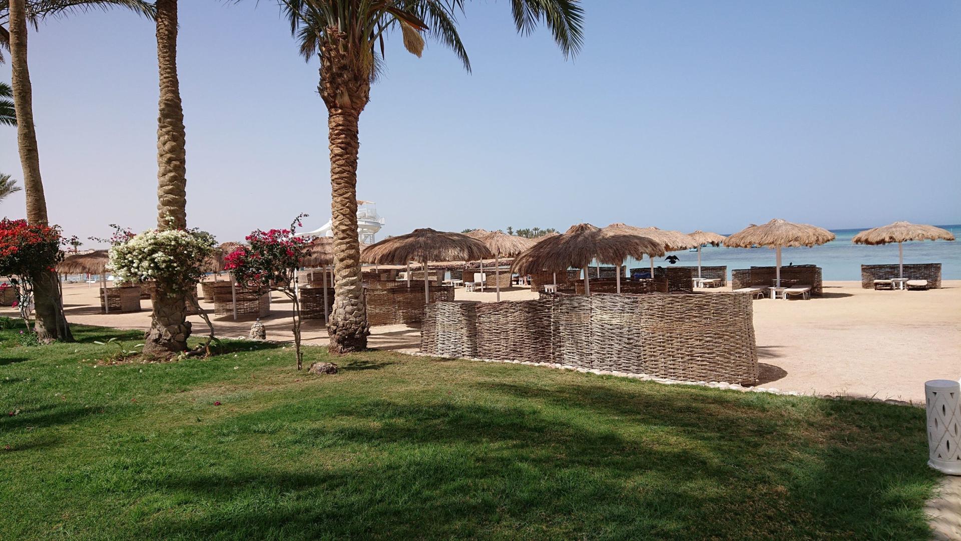 Strand des Meraki Resort Hurghada mit windgeschützten Strandkörben und Palmen am Roten Meer