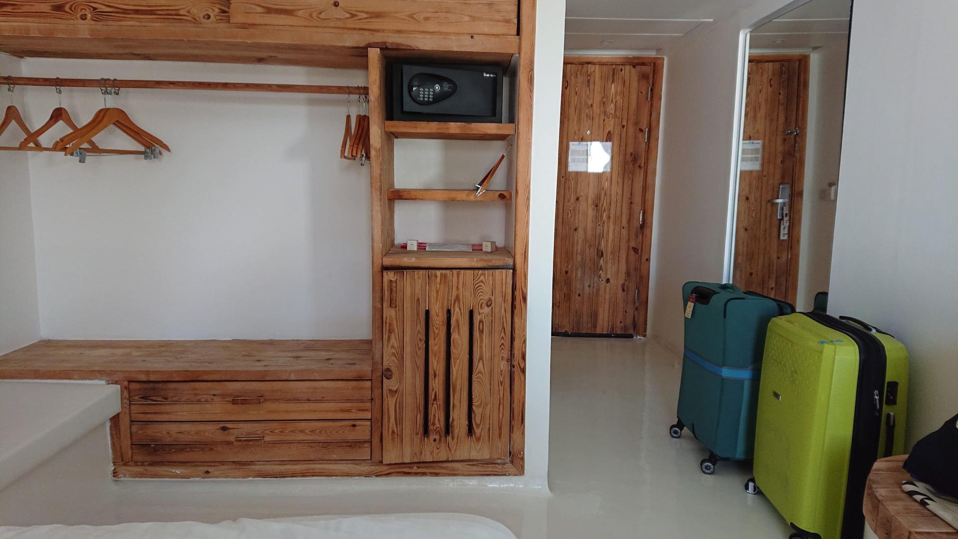 Offener Kleiderbereich mit Holzregalen, Safe und Gepäck im Zimmer des Meraki Resort