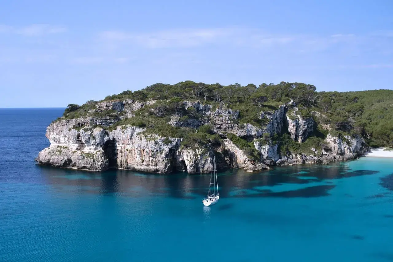 Cala Macarella auf Menorca mit türkisfarbenem Wasser, Felsküste und Segelboot