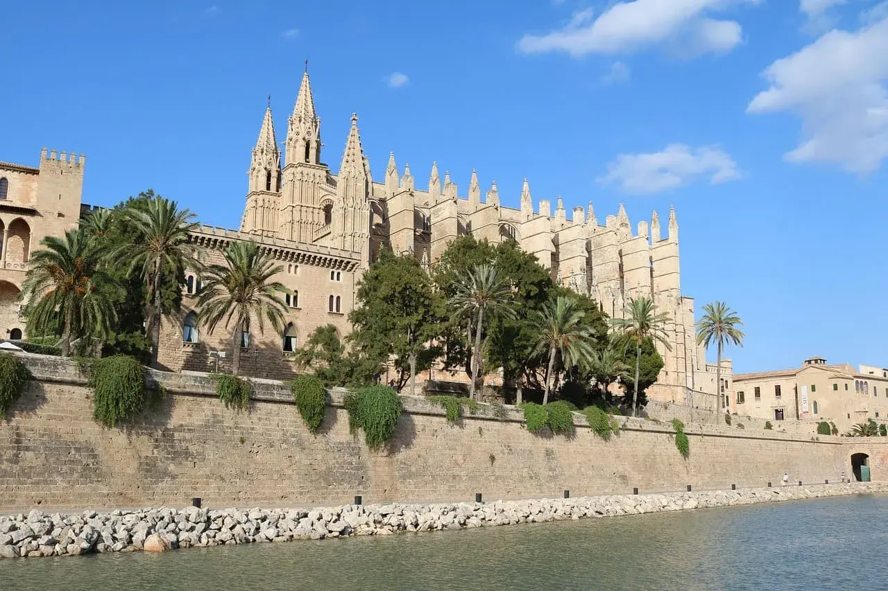 Kathedrale von Palma aus Ufernähe mit Palmen, historischer Stadtmauer und Wasserfront